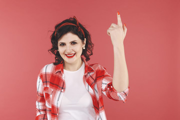 Attractive woman pointing something by her finger on the red background in the studio