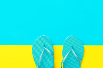 Pair of blue rubber beach slippers on duotone bright yellow cyan background. Imitation of sand and sea. Creative flat lay. Summer vacation travel relaxation tropical theme