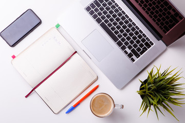 White desk with notebook, tablet, blank notebook, green flower, phone and cup of coffee.