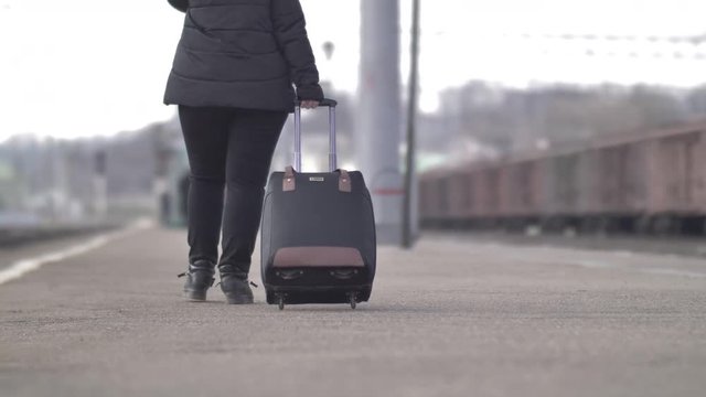 woman walks with a suitcase at the railway station in the autumn, back view, close up