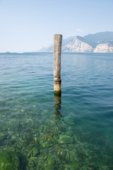 Wooden bricole for boats in the water, lake Lago Di Garda, morning light, mountains on the...
