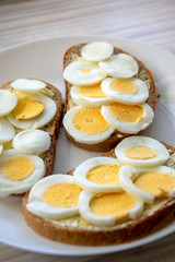 Sliced hard boiled eggs on common czech bread with butter on white plate on light wooden table