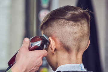 Hairdresser making a haircut to a boy with clipper. Back view. - 265015303