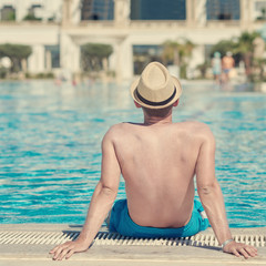 European man in sun hat on side of swimming pool on summer vacation.  Back view.