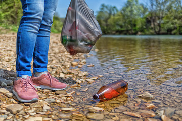 Volunteer standing on the Bank of the river, and floating in the river plastic bottle. Concept of...