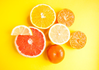 Flat lay of cut ripe juicy grapefruit, lemon and orange on yellow background. Citrus pattern.