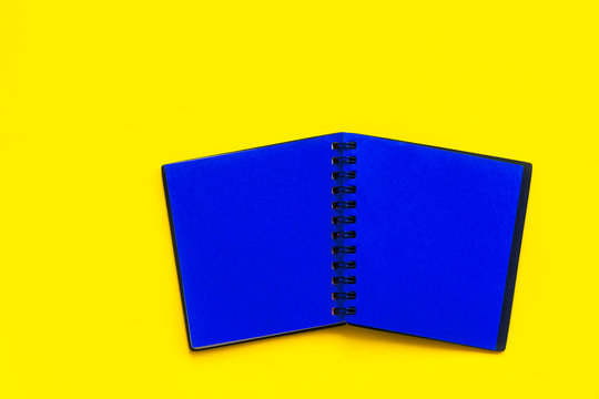 Spread Of Open Blank Black Notepad With Blue Pages On Bright Yellow Background. Trendy Funky Style Vibrant Colors. Business Education Marketing Concept. Mockup Template Design Element