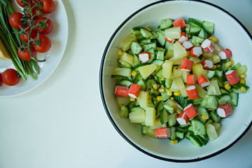 Salad with corn, crab sticks, cucumbers in a white bowl on a white background. Vegetarian salad. Cooking process.