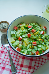 Salad with corn, crab sticks, cucumbers in a white bowl on a white background. Vegetarian salad. Cooking process.