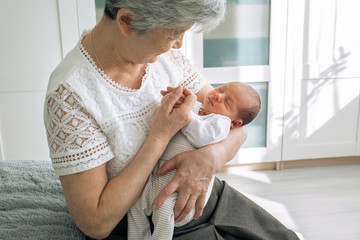 Great-grandmother plays with a newborn great-granddaughter. A grandmother with gray hair is nursing...