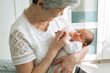 Great-grandmother holds a newborn great-granddaughter in her arms. A grandmother with gray hair is...