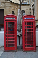 Two red characteristic telephone box on street, behind building