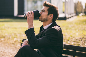 Elegant businessman enjoys drinking coffee while sitting outdoor.Toned image.