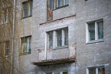 Broken concrete balcony on the facade of the building. Restoration of an old residential gray plastered house. Wooden windows and exit with door.