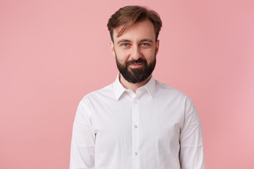Portrait of young calm handsome bearded man, wearing a white shirt. Looking at the camera and smile...