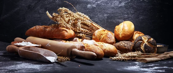 Fotobehang Bakkerij Assortiment van gebakken brood en broodjes op rustieke zwarte bakkerijtafelachtergrond
