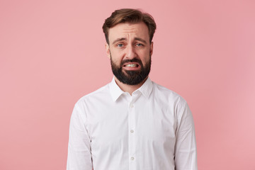 Portrait young bearded man who saw a spider. Looks with disgust isolated over pink background.