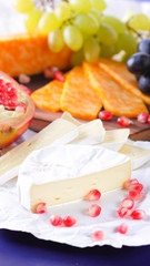 Different types of cheese and fruit. Sliced camembert and pomegranate. Soft and hard cheese and nuts. Camembert and grapes on blue background. Vegetarian food