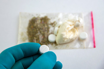 Fototapeta na wymiar synthetic drugs: laboratory assistant holds a pill in his hand against the background of samples of narcotic herbal preparations