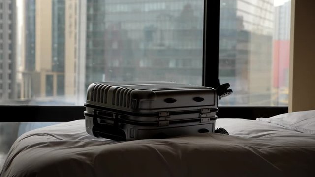 Traveller case fly and tumble down on bed at hotel room, super slow motion shot. Plastic bag thrown on blanket by guest, check-in after long flight. Modern city buildings blurred on background