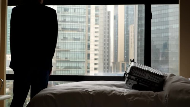 Guest man enter hotel room, throw bag on bed and weary sit down near, black silhouette against window. Tired business man arrive at accommodation after long trip of flight