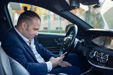 a businessman in tha jacket standing sitting in the car holding mobile phone