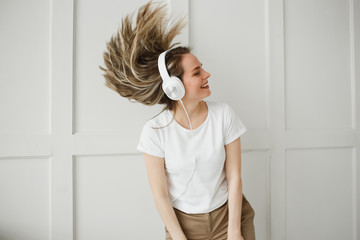 Fototapeta na wymiar Enjoy the music. Happy young woman pleasing music in white headphones. She clothed in white T-shirt and beige pants.
