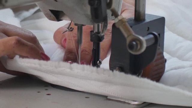 Close up on woman sewing white blanket in mattress factory