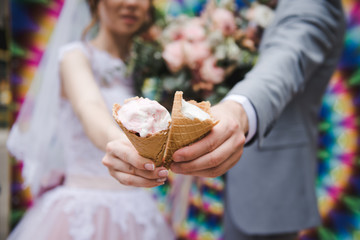The bride and groom are eating ice cream together on a bright wall background. Funny newlyweds eat...