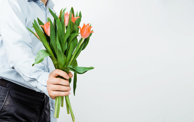 The man is holding in the hands of red tulips on a light background. The concept of handing flowers to a woman, girl. A man wearing a shirt is holding flowers in his hands.