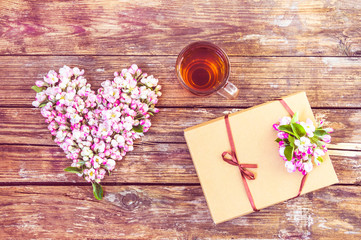 a heart of flowers and buds of an apple tree, a cup of tea, a box with a gift, sweets in a box. on old wooden background