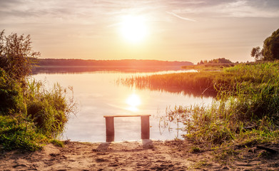 Empty bench near the river at sunset. Away from the hustle and bustle. Sun setting over the...