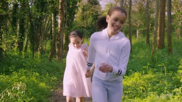 Beautiful young girls holding hands and skipping through a forest, in slow motion