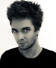 Portrait of a young handsome man with tousled and hair sprayed hair, stubble beard and slightly turned face a side on a white background in black shirt.