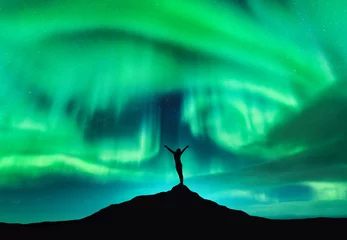 Keuken spatwand met foto Aurora borealis and silhouette of a woman with raised up arms on the mountain peak. Lofoten islands, Norway. Aurora and happy girl. Starry sky and polar lights. Night landscape with aurora and people © den-belitsky