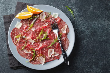 Marbled beef carpaccio with arugula, lemon and parmesan cheese on dark concrete table. Top view, flat lay with copy space