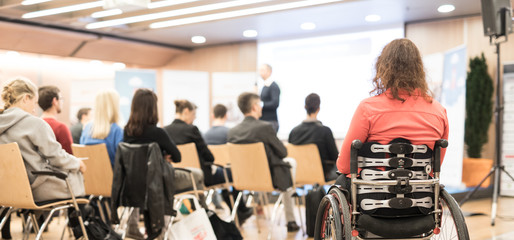 Rear view of unrecognizable woman on wheelchair participating in business conference talk. Business...