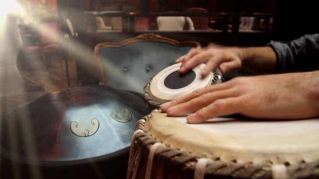 A man playing an ethnic musical instrument tabla in the interior of the lounge, with the rays of the sun from window
