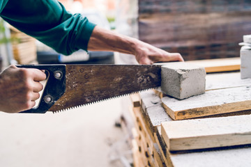 Close up on the construction worker using the hand saw to manually cut the brick insulation material concrete stone