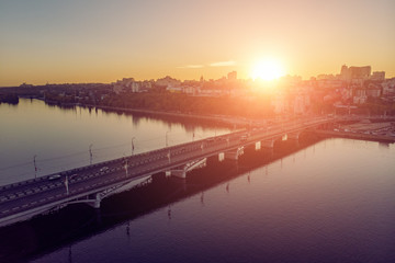 Aerial view of Chernavsky bridge over river with reflection, car traffic and Voronezh city with buildings at sunset background, urban transportation