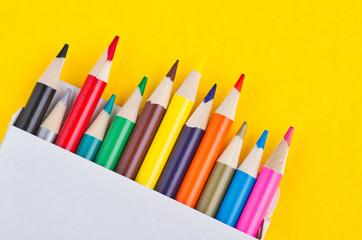 close-up image of colourful pencils in the white box over yellow background