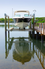 Small clean v-bottom bay motorboat on an electric lift on a wood dock with boat reflection in the...