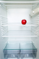 Bright fresh red apple on shelf of open empty refrigerator. Weight loss diet concept.