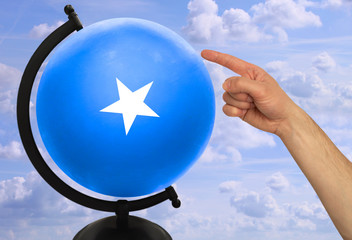 The index finger of a male hand points to a globe with a colored national state flag somali