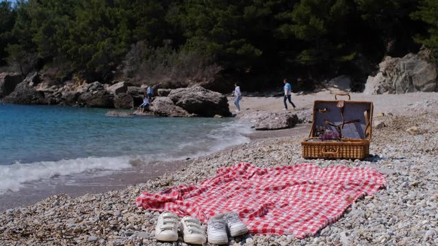 Closeup of summer picnic basket with water, fruit and croissant near sea. Family running together