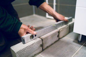 Construction worker craftsman using spirit level tool in order to check cement bricks installing in bathroom before laying ceramic tiles