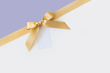 Fototapeta premium Gold ribbon with a bow as a gift on a white and lavender background