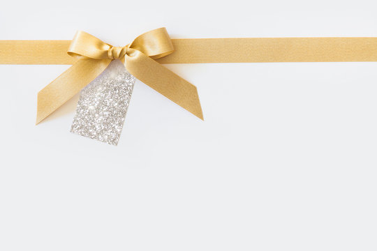 Gold ribbon with a bow as a gift on a white background. Empty paper name tags shiny colors