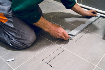 Construction worker craftsman measuring tiles on the floor before installation of the glass tile protective wall equipment