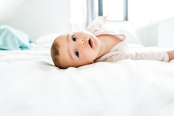 6 month old baby looking at camera in the morning lying on the bed between white sheets.